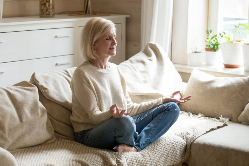 Woman over 50 meditating in jeans on her bed
