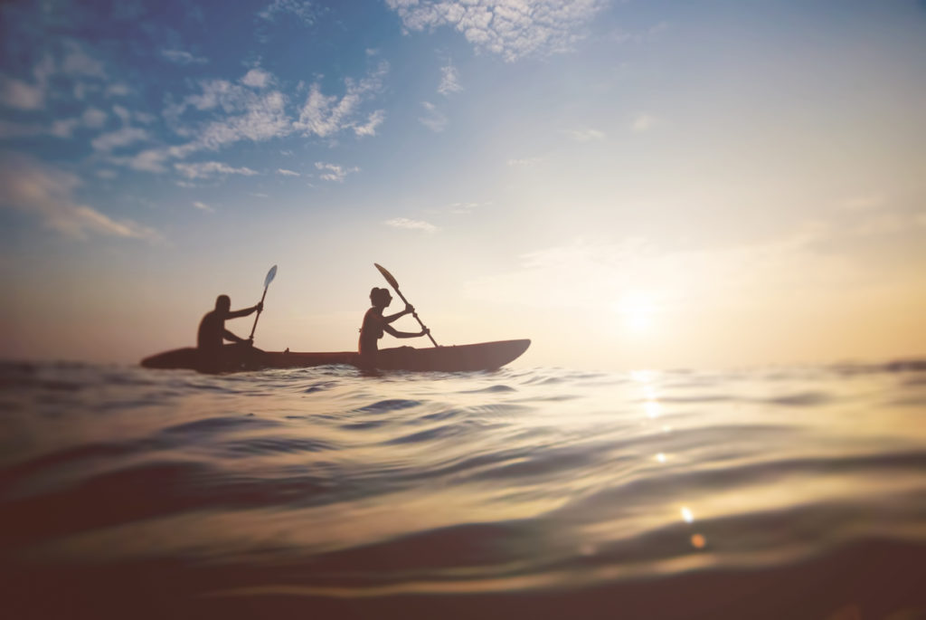 Two people kayaking on ocean with sunset in view.