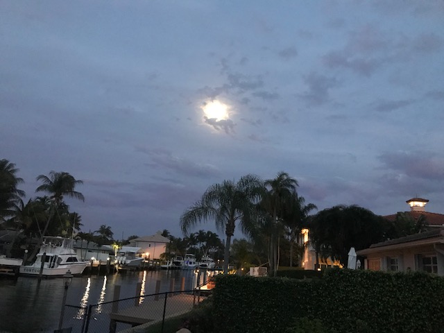 The moon peaks through the clouds over the water